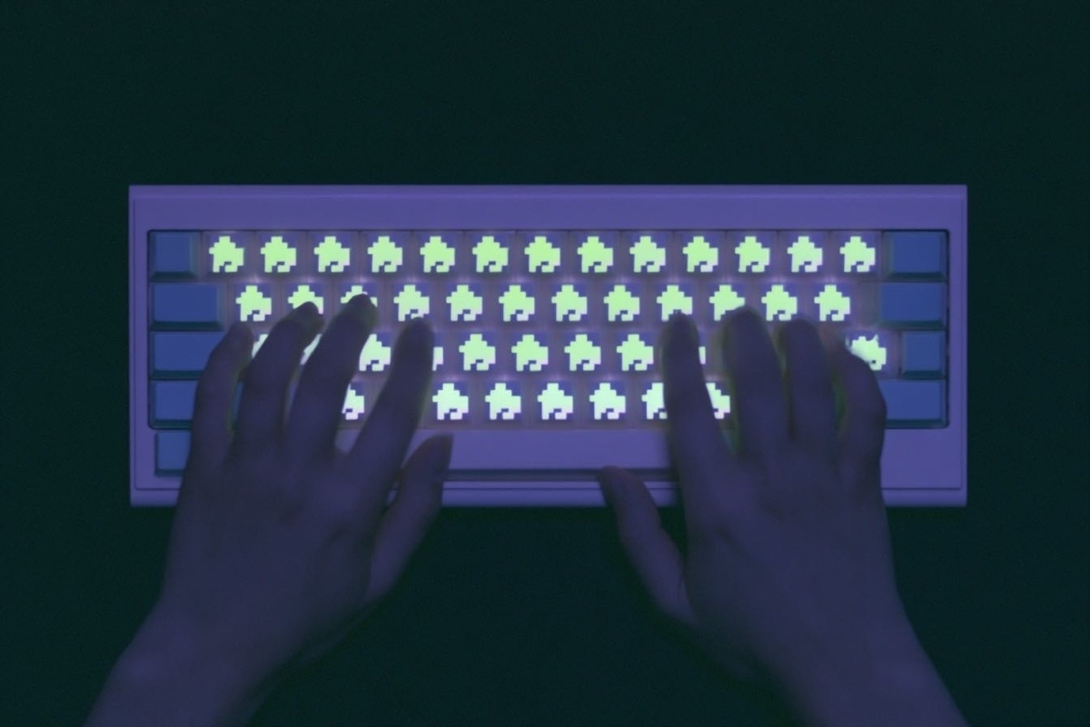 Hands typing on a glowing keyboard in the dark, each keycap lit with a pixel-art space invader