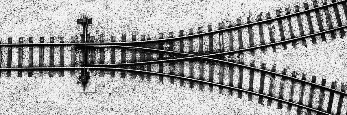 Railroad tracks crossing and diverging over pale gravel.