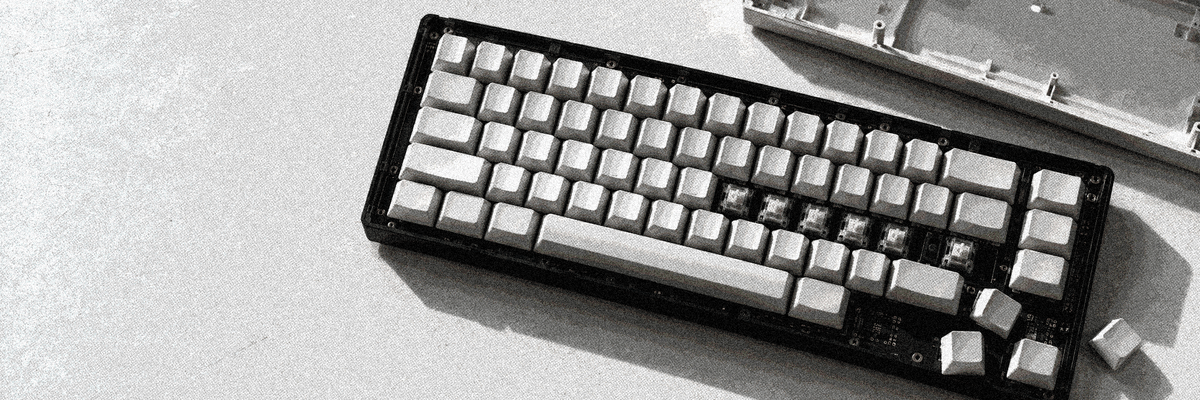 A partially disassembled keyboard with blank keycaps and exposed switches on a pale tabletop.